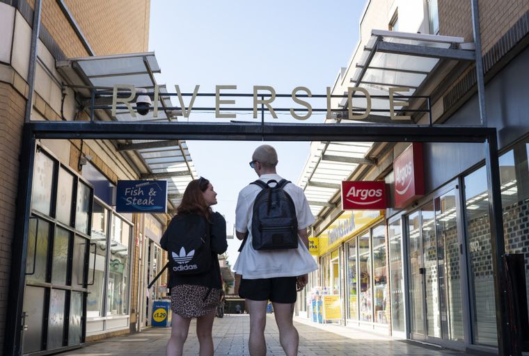 A shopping arcade with 'Riverside' signage and two people walking away from the camera.