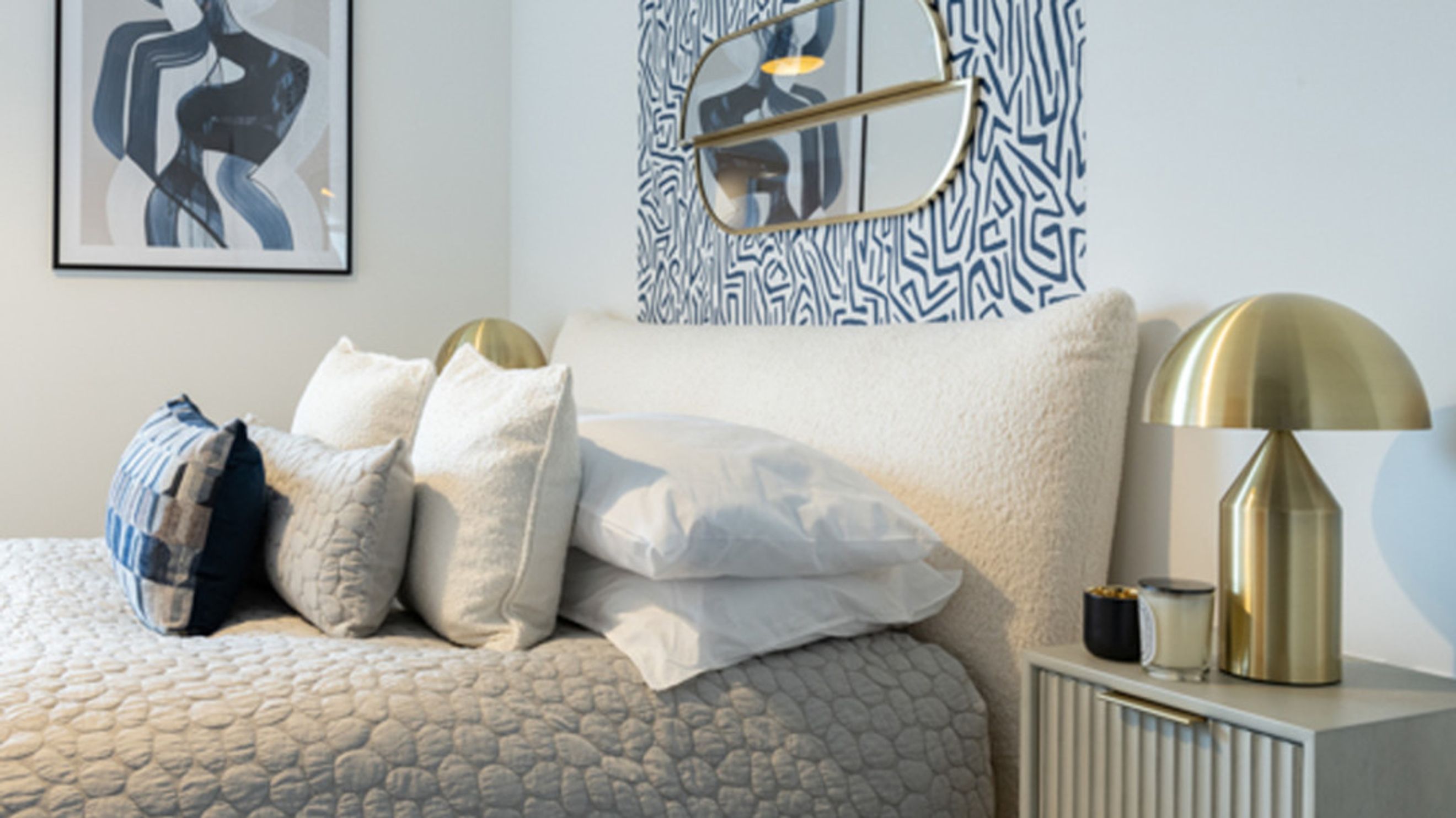 A bedroom with a bed, pillows, a bedside lamp, and artwork.