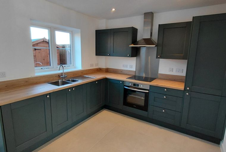 A modern kitchen with dark green cabinets, wood countertops, a double sink, and a stainless steel oven and extractor fan.