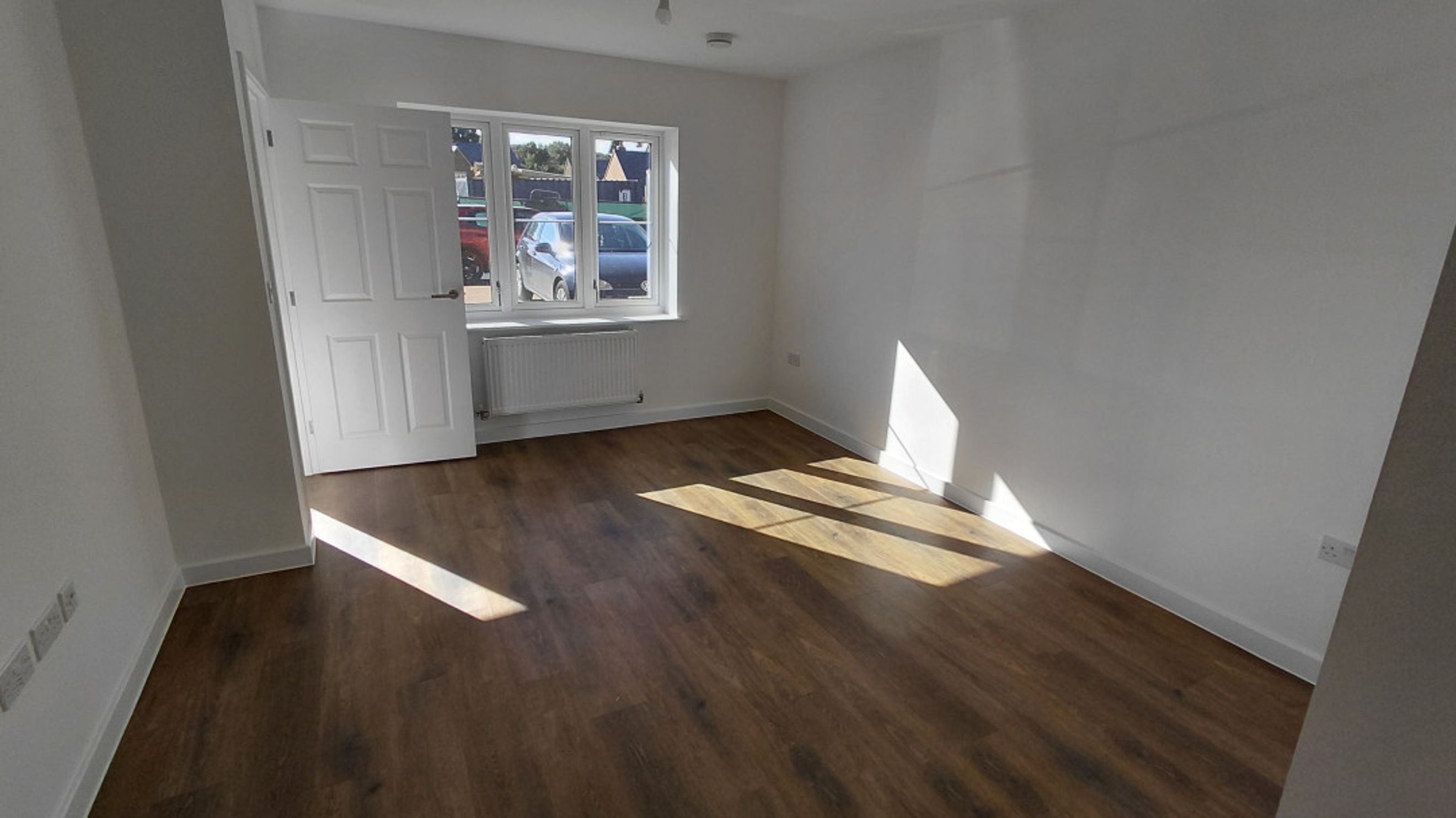 A room with a white door, a window, and wood-effect flooring.