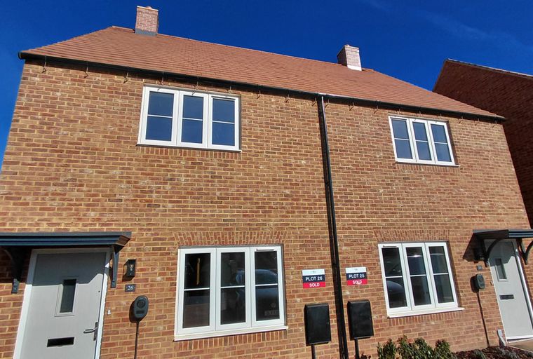 A new build semi-detached house with brick exterior and white-framed windows.