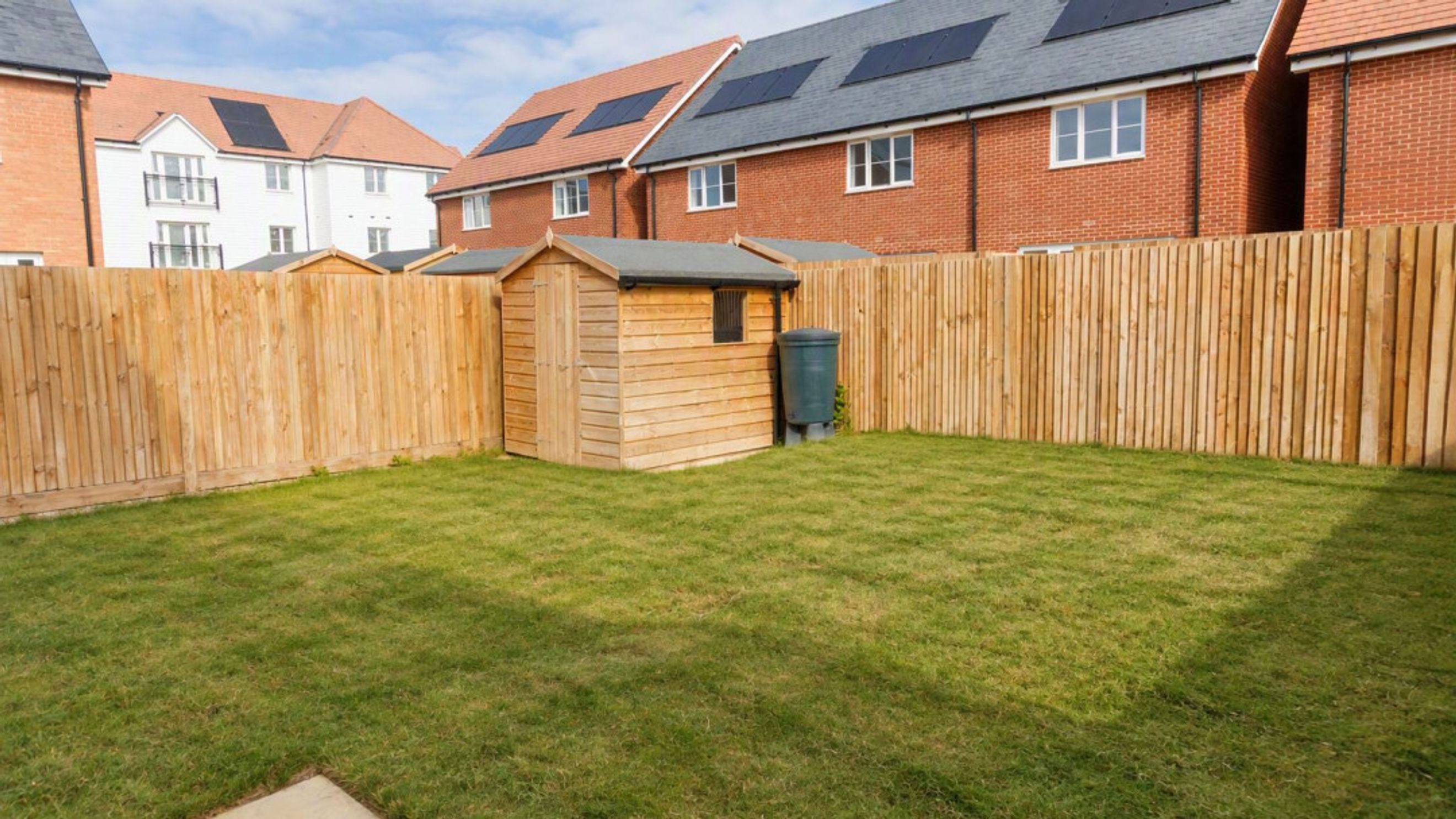 A backyard with a wooden shed, a water butt, and a wooden fence.