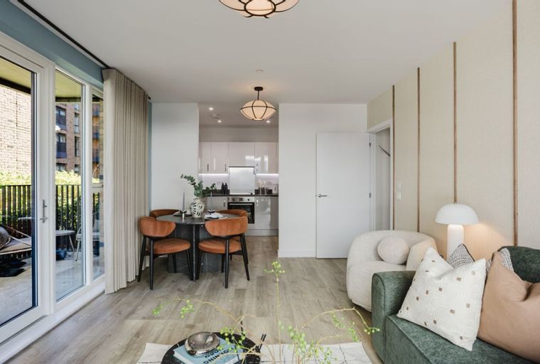 A living room and dining area with a kitchen in the background, featuring a sofa, chairs, and a table.
