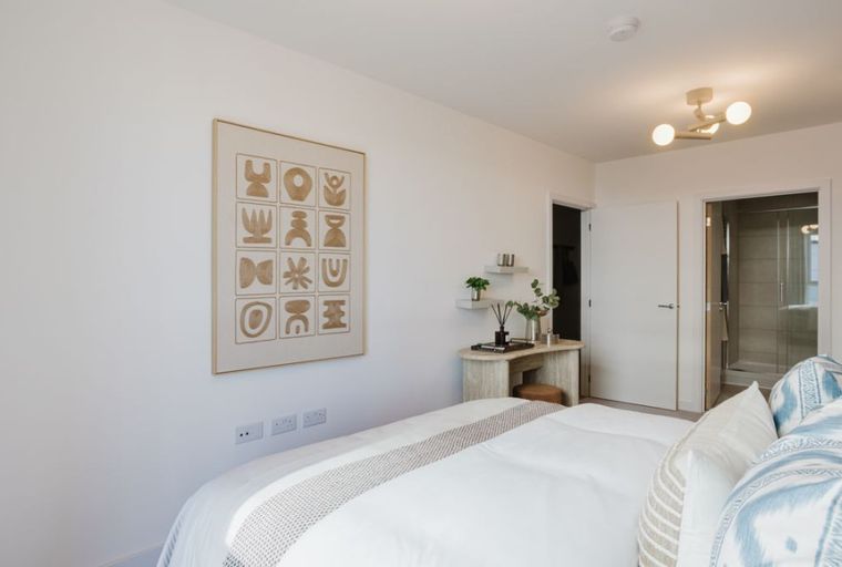 A bedroom with a bed, abstract art, a vanity, and an adjacent bathroom.
