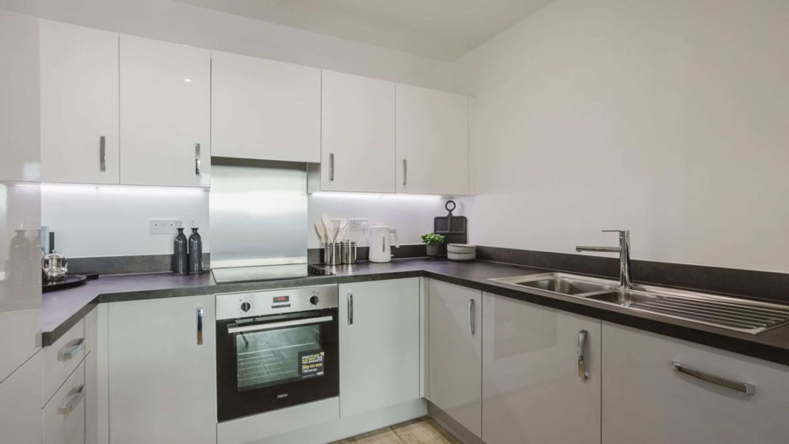 A modern kitchen with white cabinets, a stainless steel backsplash, an oven, and a sink.