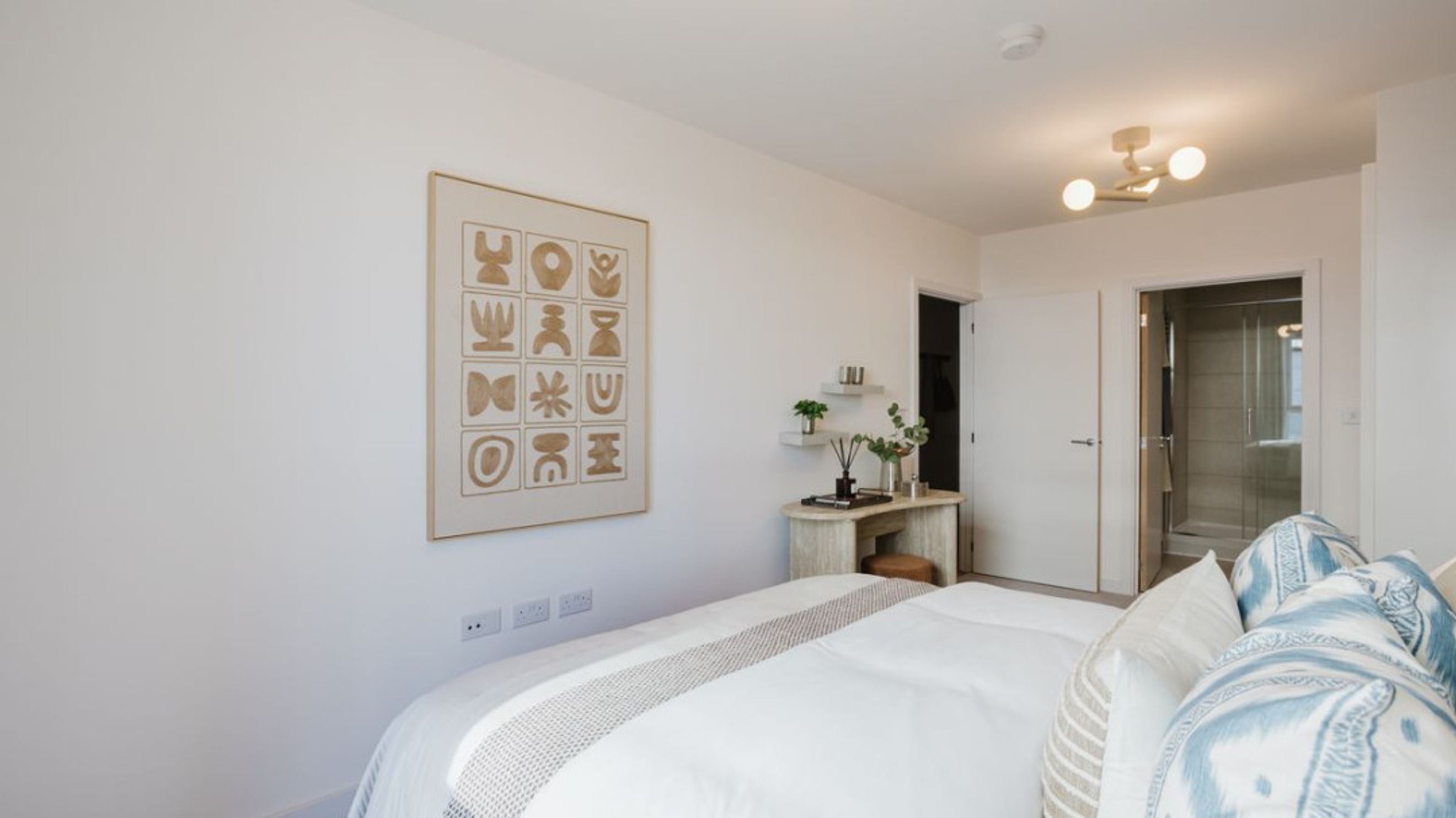 A bedroom with a bed, abstract art, a vanity, and an adjacent bathroom.