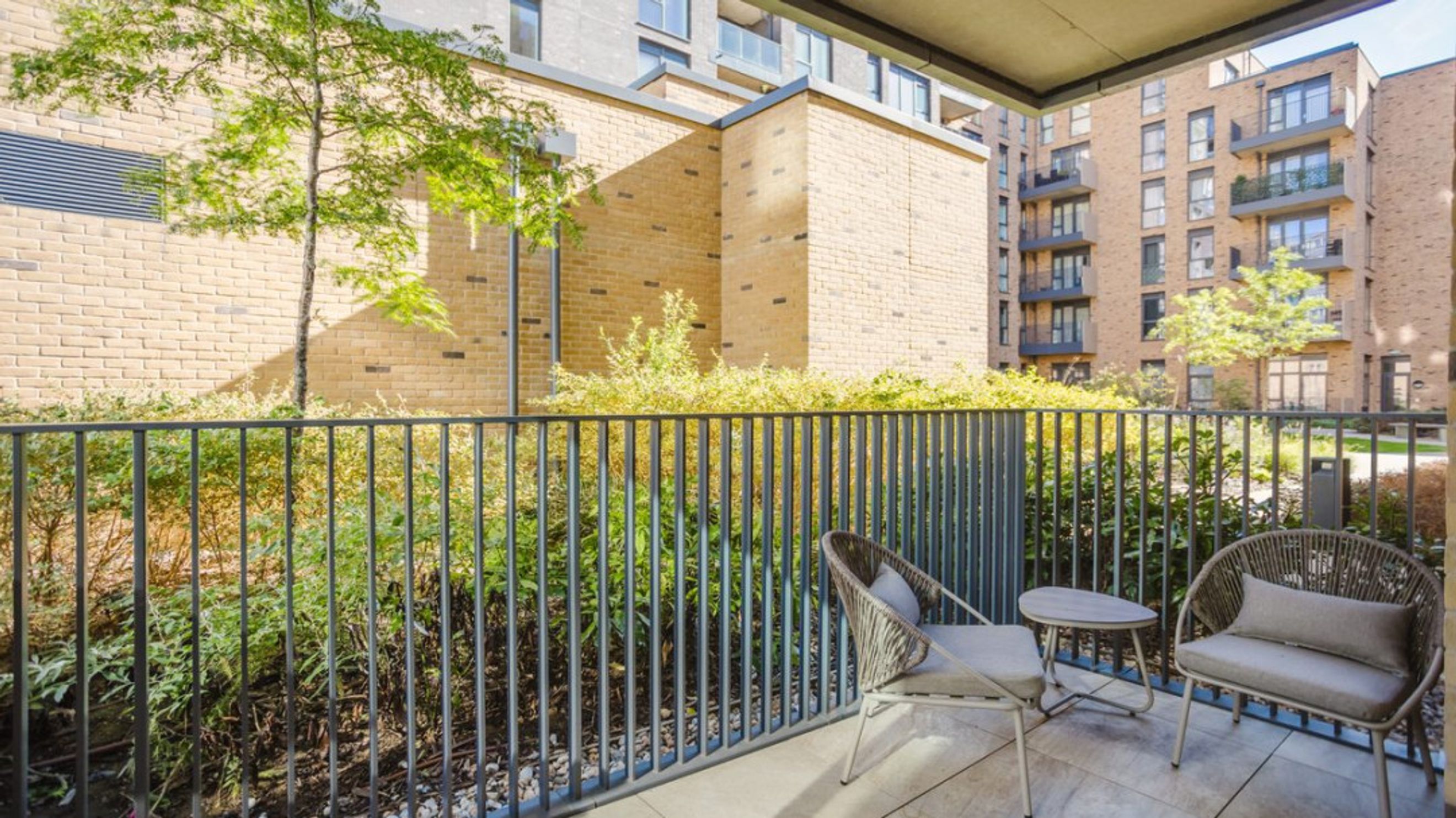 A balcony with two chairs and a table overlooking greenery and apartment buildings.