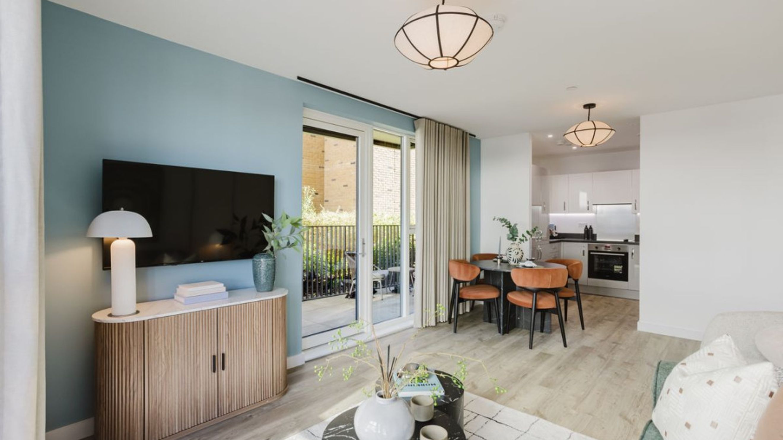 A living room and kitchen area with a dining table and chairs, a television, and a balcony.