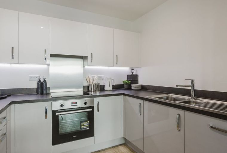 A modern kitchen with white cabinets, a stainless steel backsplash, an oven, and a sink.
