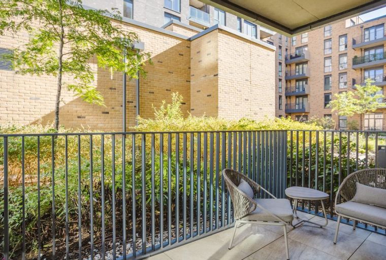 A balcony with two chairs and a table overlooking greenery and apartment buildings.