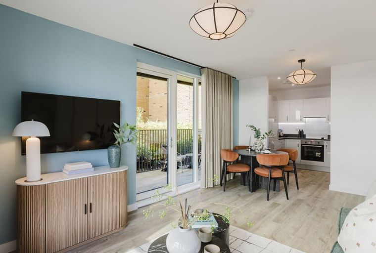 A living room and kitchen area with a dining table and chairs, a television, and a balcony.