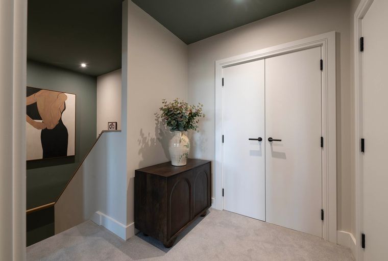 A hallway with a dark wood cabinet, a vase of flowers, a painting, and white doors.