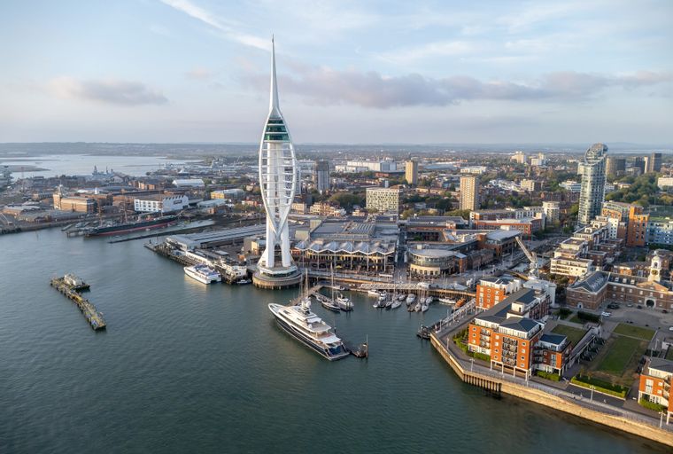 An aerial view of a modern waterfront city with a tall tower and many boats docked in the harbor.