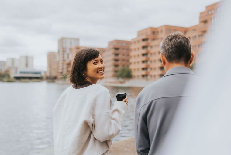A woman and a man standing by a body of water with buildings in the background.