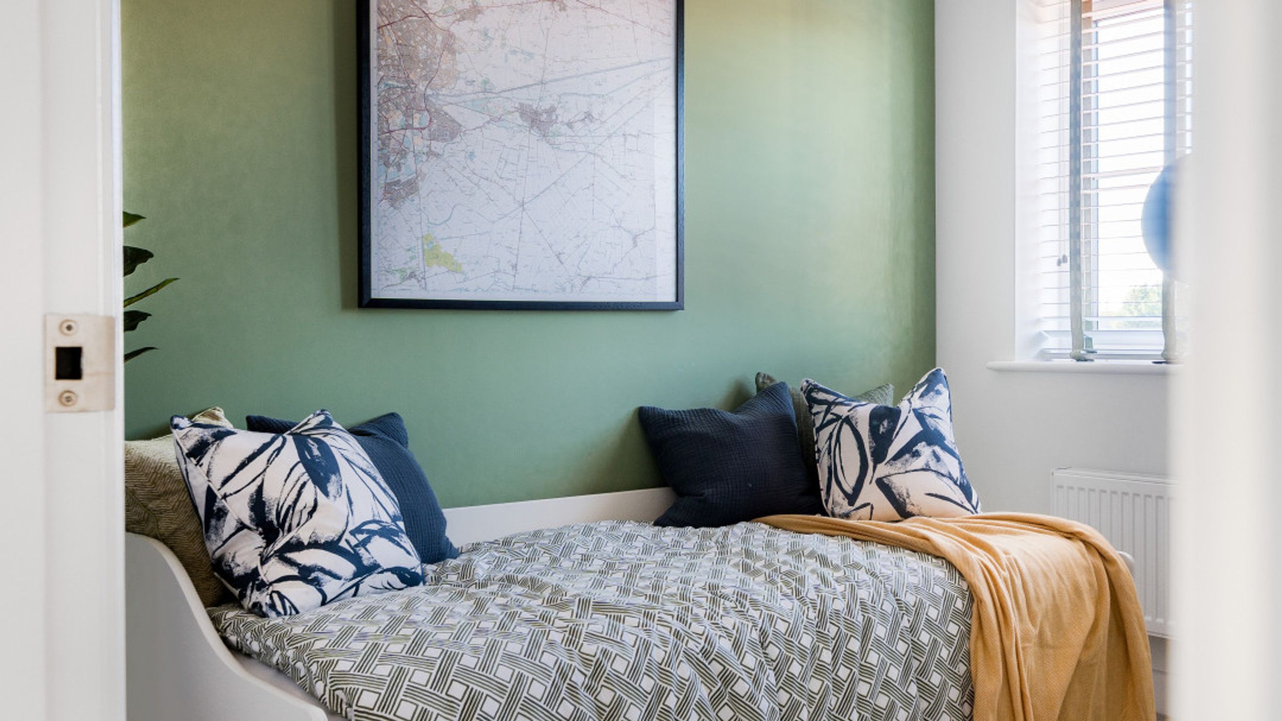 A bedroom with a bed, pillows, a blanket, a map on the wall, and a window.