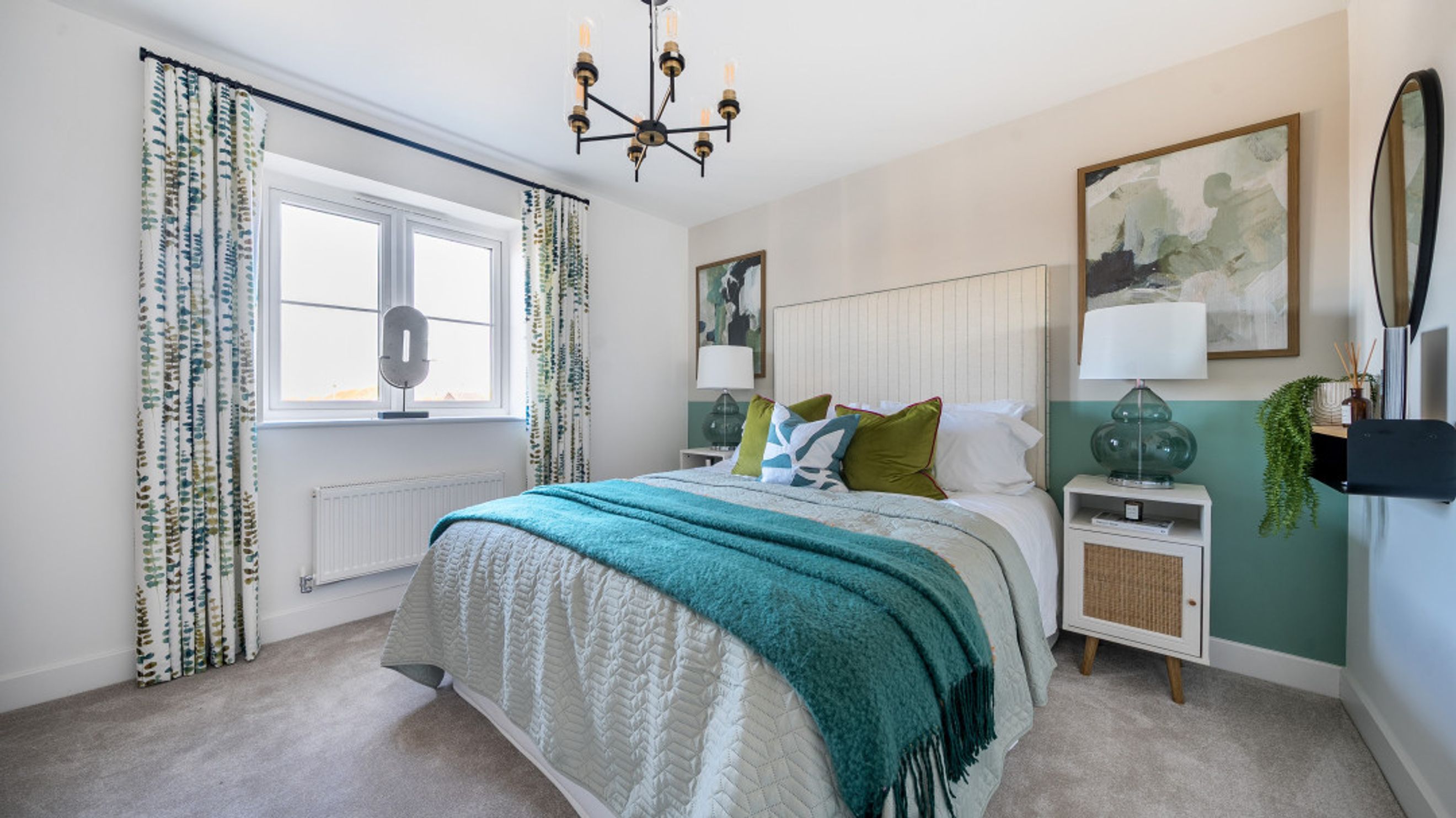 A bedroom with a bed, pillows, a teal throw, bedside tables, lamps, curtains, and artwork.