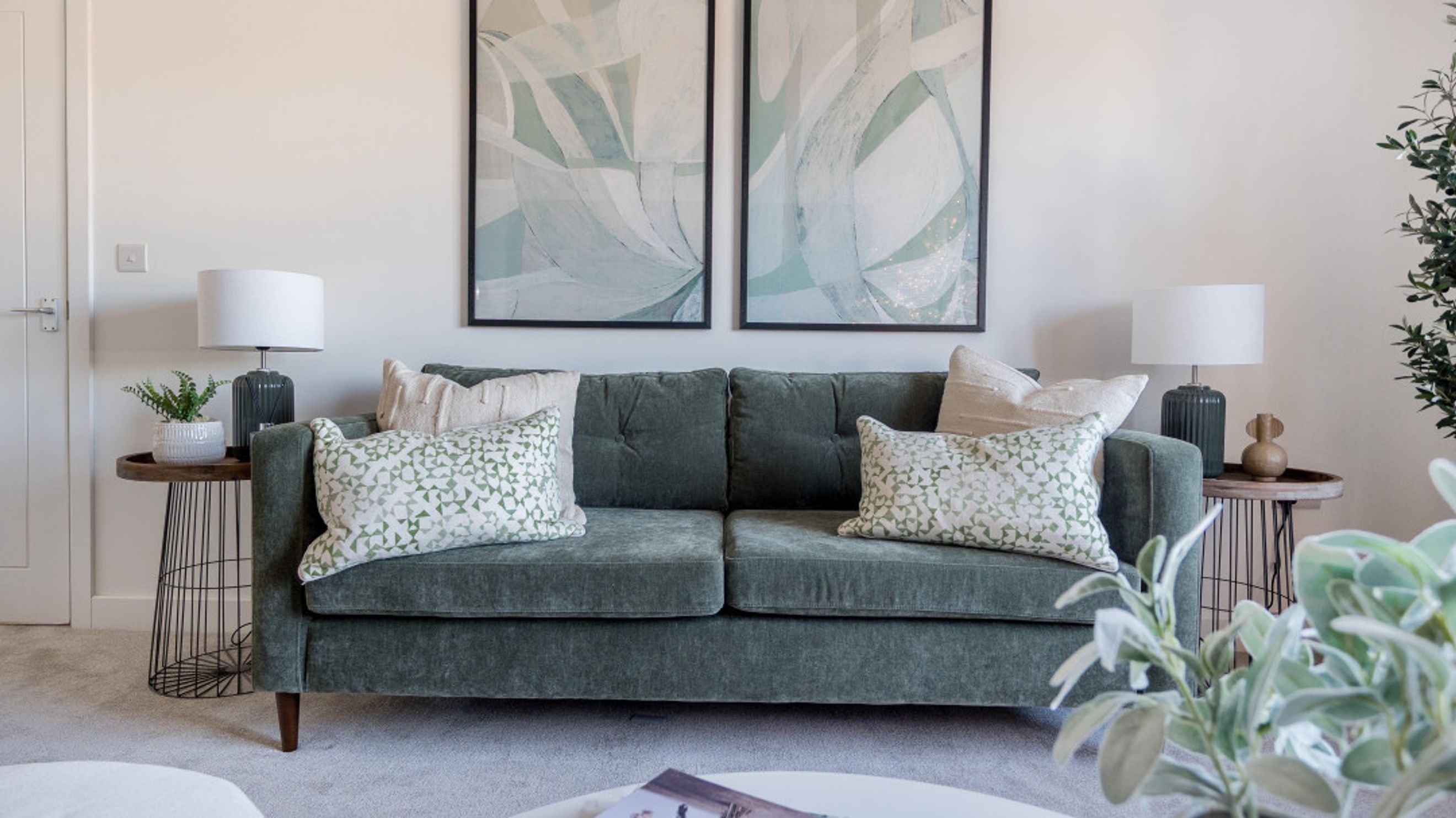 A living room with a green sofa, two table lamps, and two pieces of abstract art on the wall.