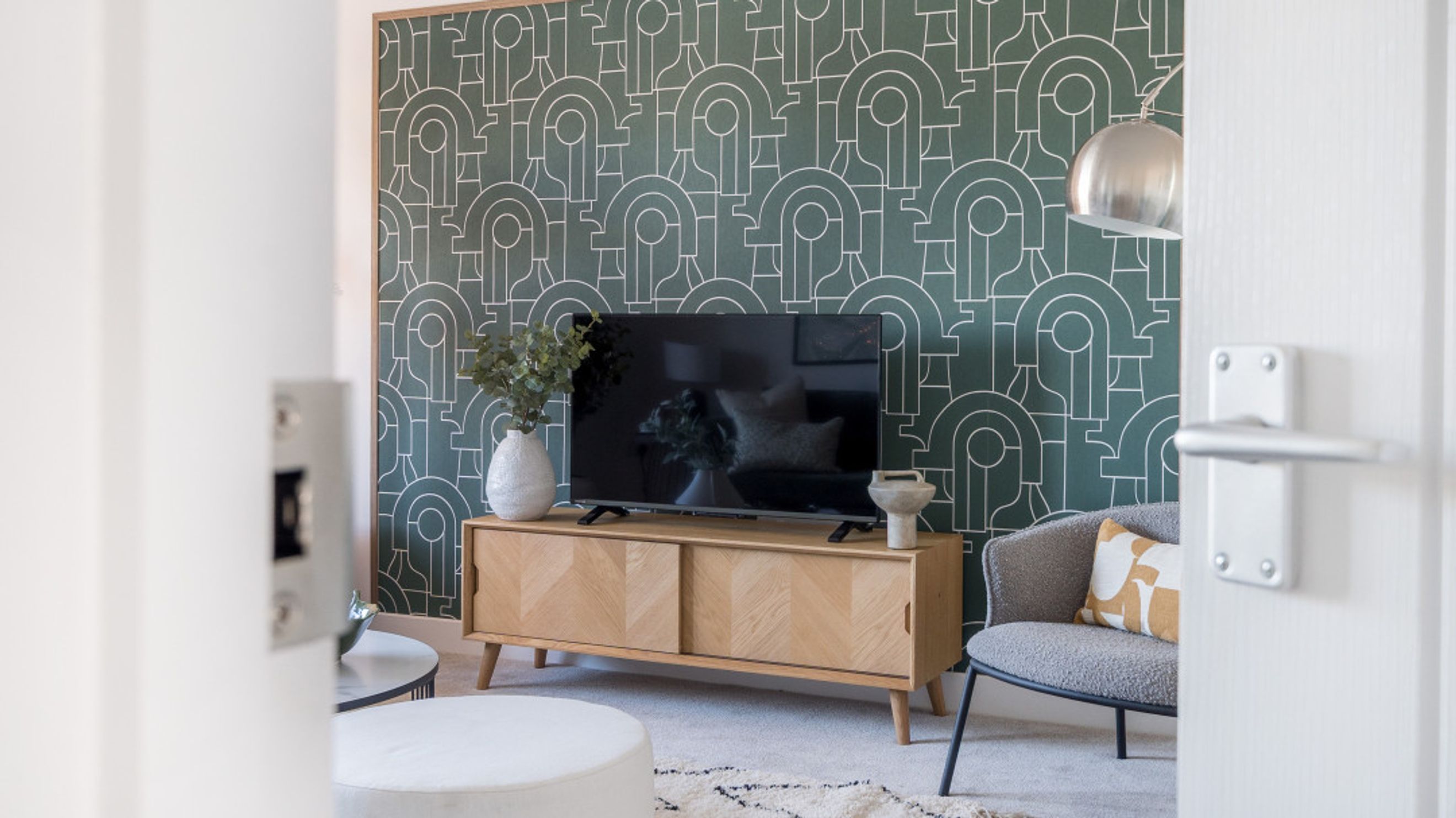 A living room with a TV on a wooden media console and a patterned wallpaper.