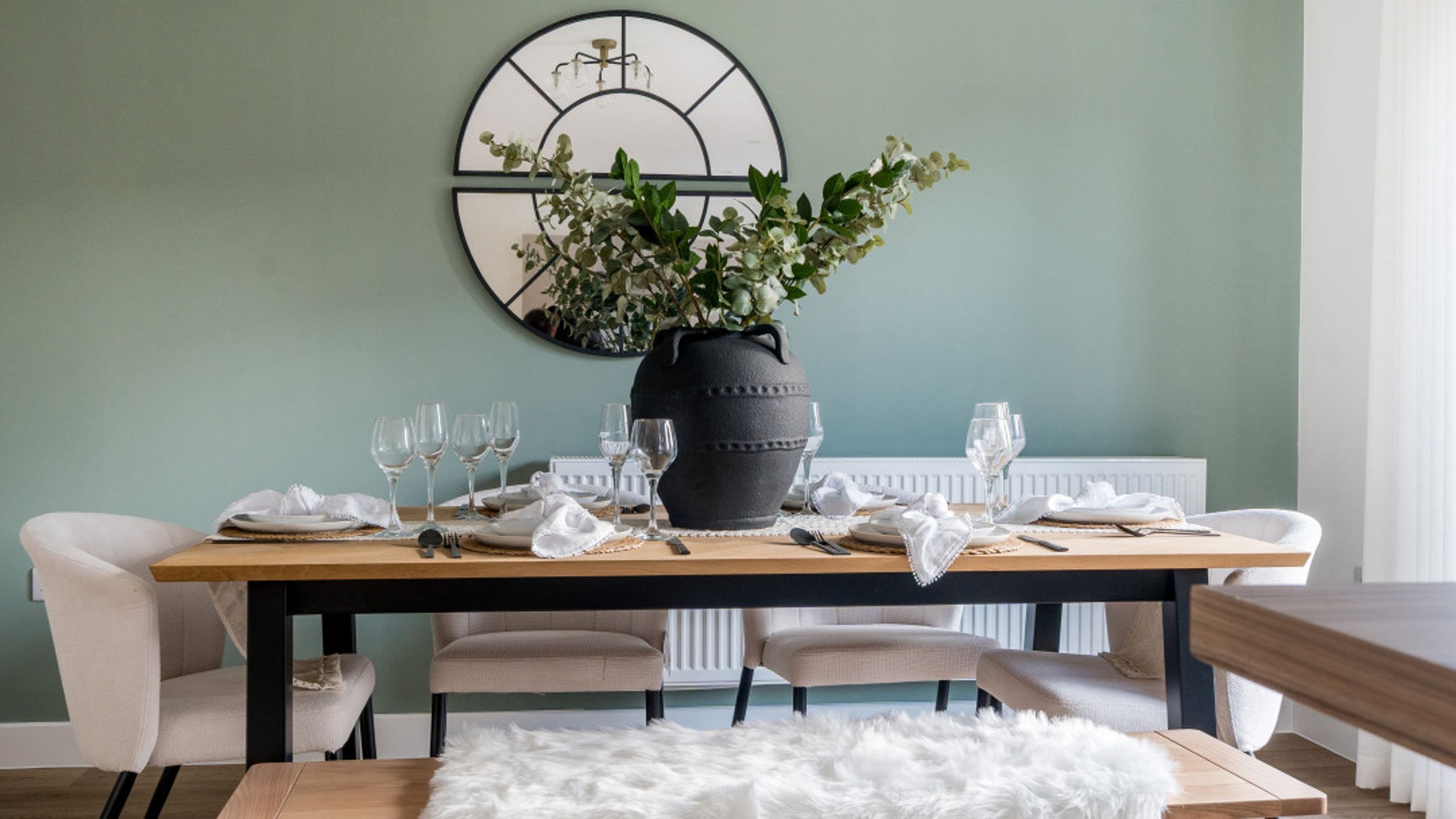 A dining table set with plates, glasses, and a large vase of greenery.