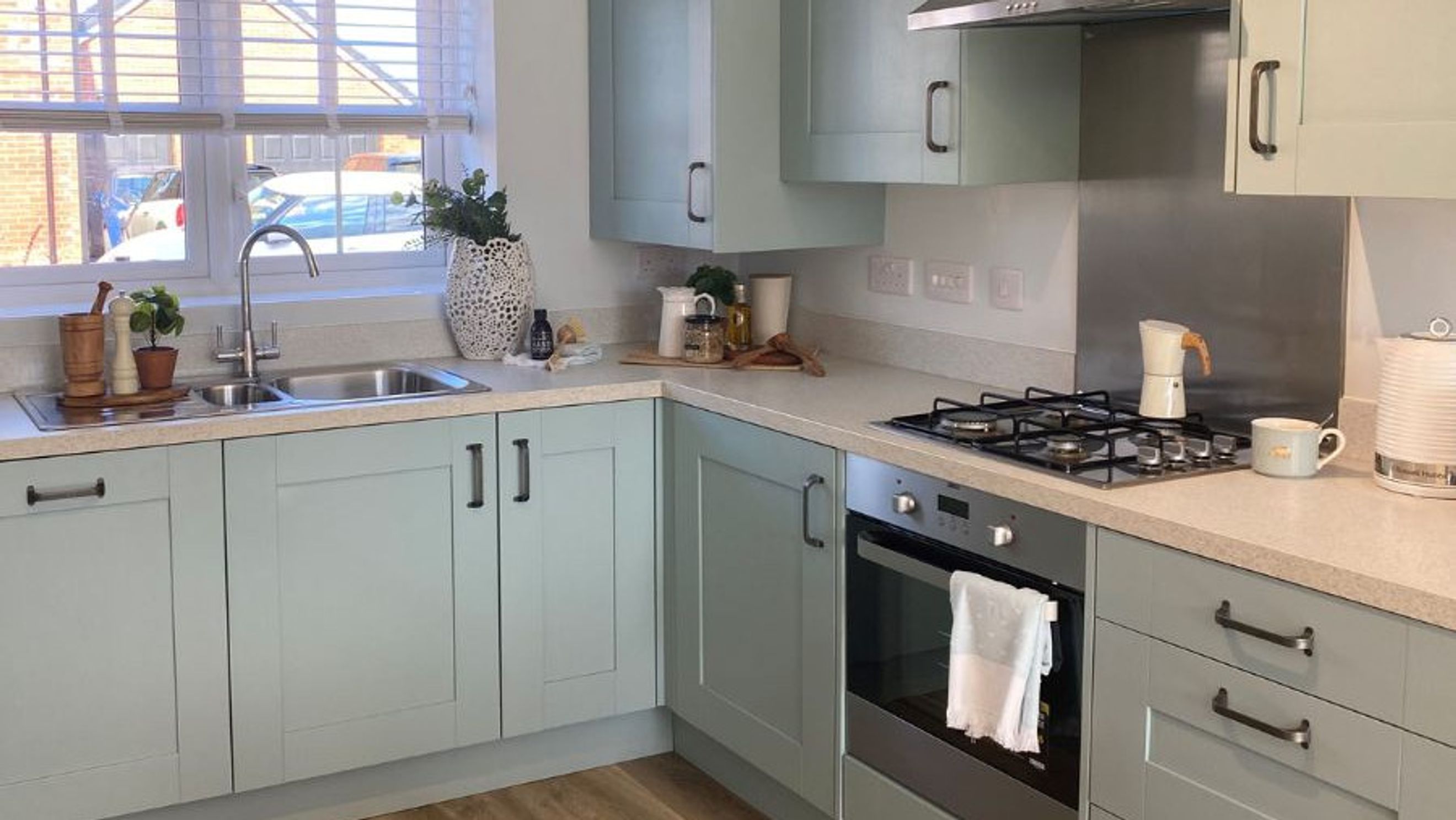 A kitchen with sage-green cabinets, a sink, and a gas stove.