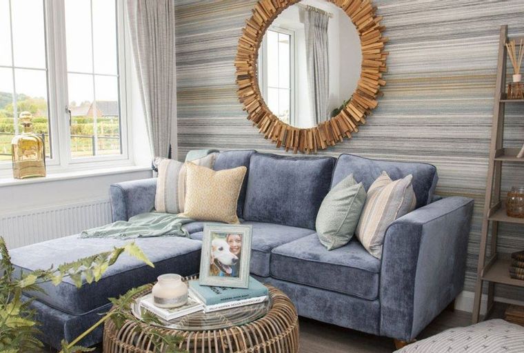 A living room with a blue sectional sofa, a round mirror, and a ladder shelf.