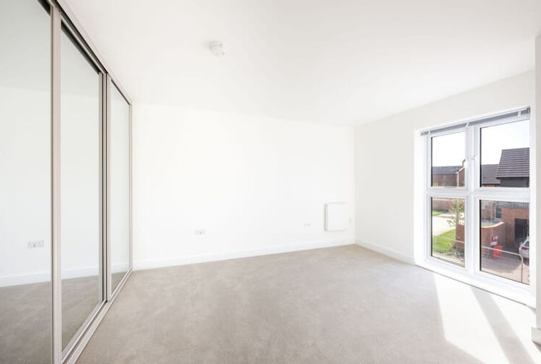 A bedroom with a mirrored wardrobe and a window.