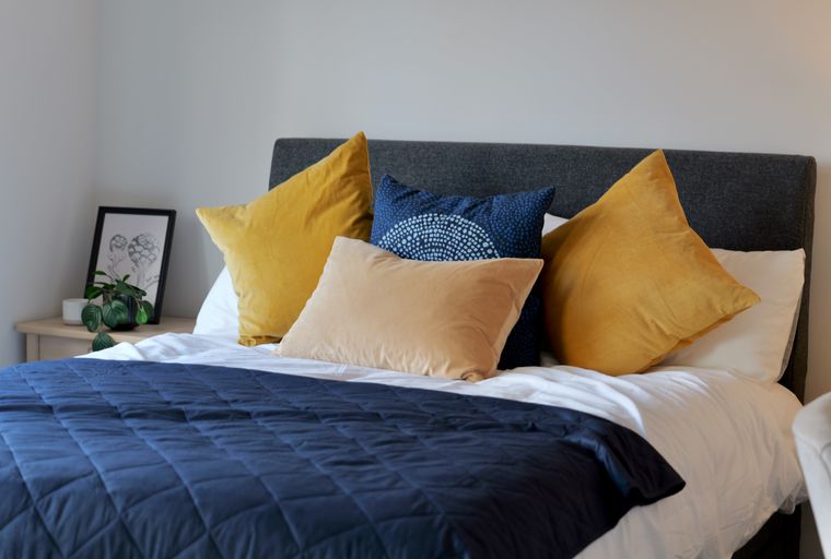 A bedroom with a bed, pillows, and a dark blue quilt.