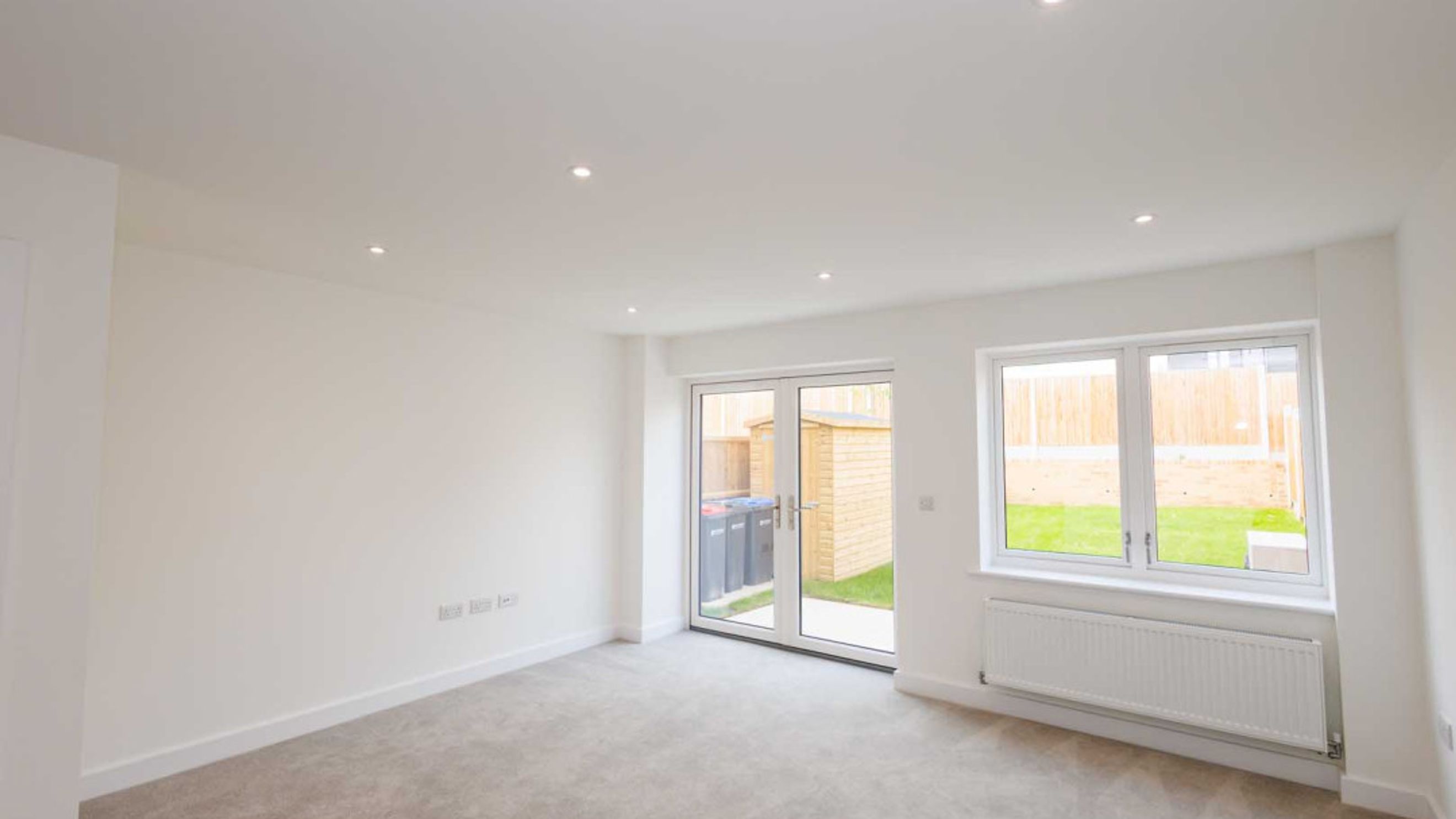 A living room with double doors leading to a garden and a window overlooking the garden.