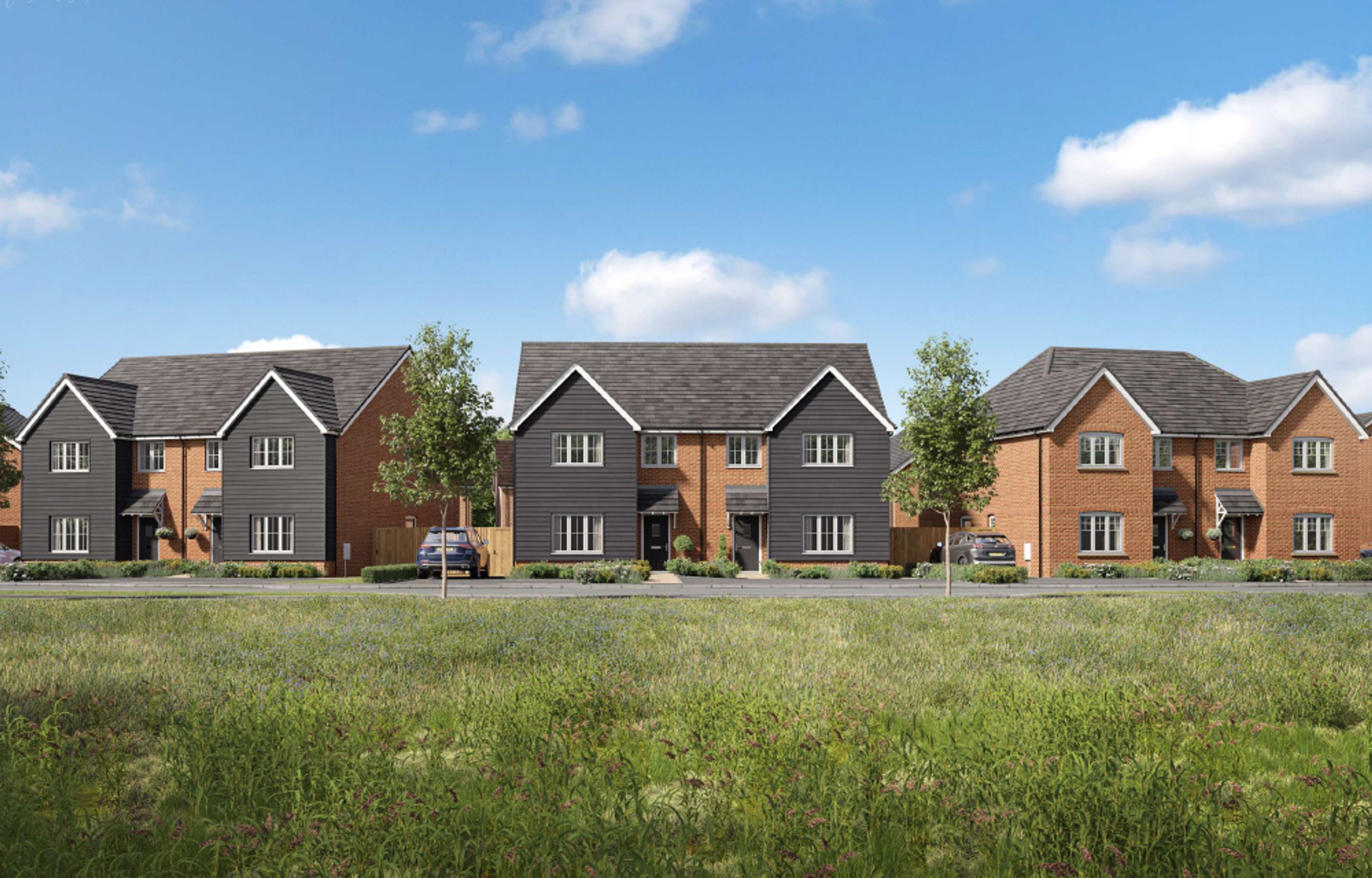 A row of modern houses with dark grey cladding and brick exteriors under a blue sky with clouds.