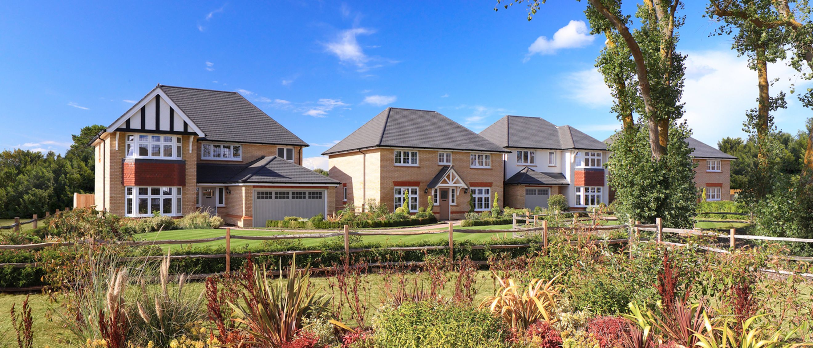 A row of modern houses with gardens under a blue sky.