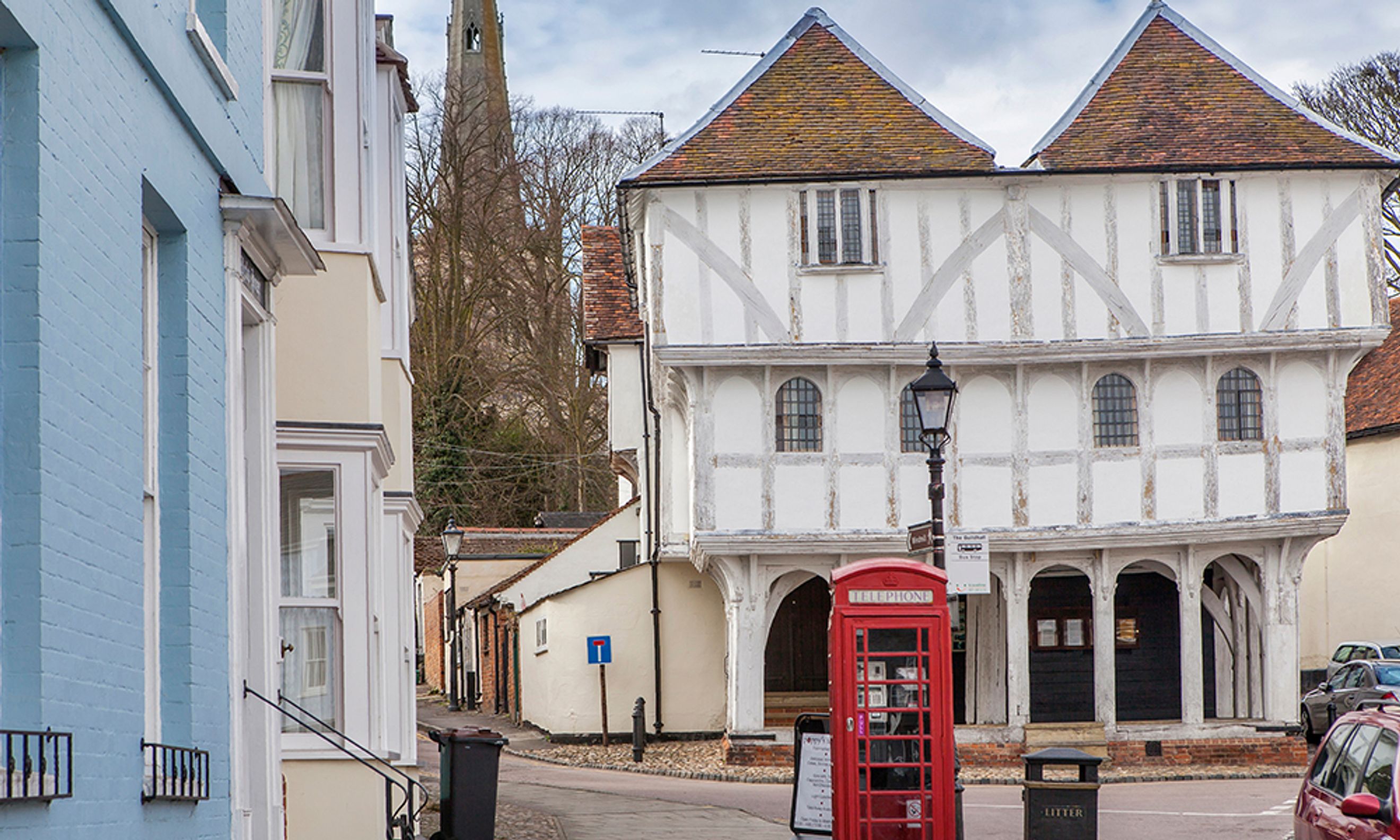 A red telephone booth stands on a street in front of a historic timber-framed building.