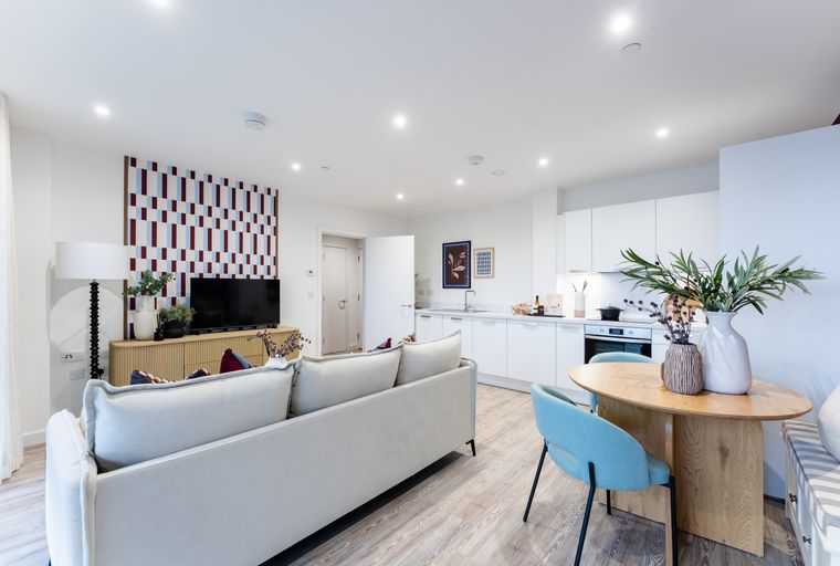 A living room and kitchen area with a sofa, dining table, and kitchen cabinets.