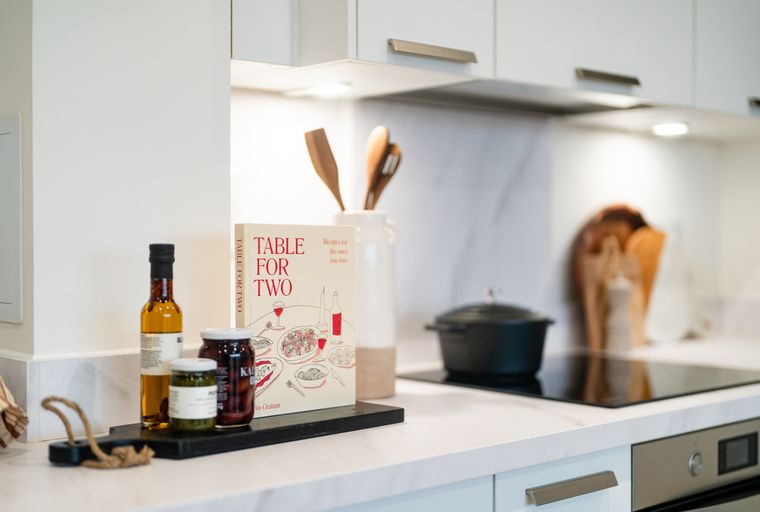 A kitchen counter with a cookbook, jars of food, and a bottle of oil.