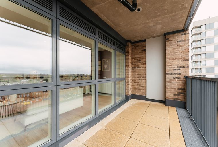 A balcony with large windows, brick walls, and tiled flooring.