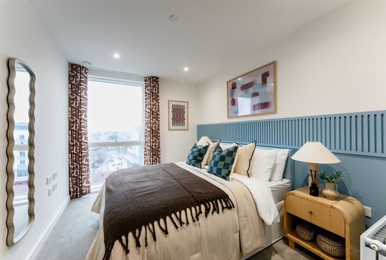 A bedroom with a bed, pillows, curtains, and a bedside table.