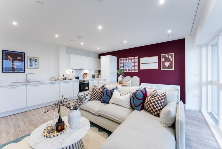 A living room and kitchen area with a sectional sofa and white cabinets.